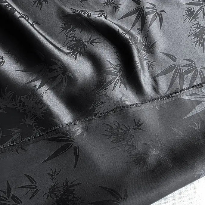 The Bamboo Jacquard Mulberry Silk Fabric by Longan Craft is a colorful rayon silk fabric with a smooth, glossy bamboo leaf pattern and a visible diagonal stitched seam. Slightly wrinkled, it's ideal for cozy silk lining.