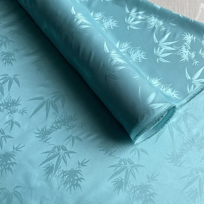 A partially unrolled roll of Longan Craft Bamboo Jacquard Mulberry Silk Fabric By The Yard displays a subtle bamboo leaf jacquard pattern and glossy texture, perfect as colorful rayon silk fabric or cozy silk lining fabric.