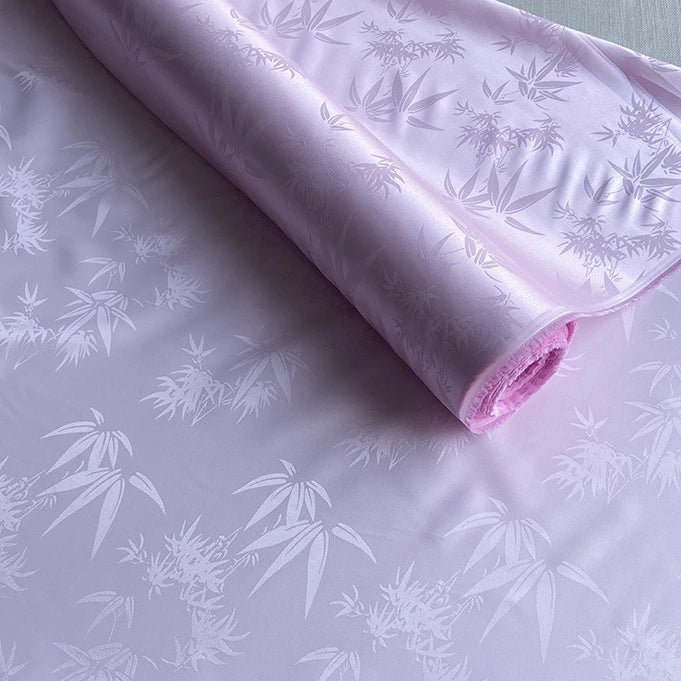 A roll of Longan Craft's Bamboo Jacquard Mulberry Silk Fabric is partially unrolled, showing its silky jacquard texture and elegant sheen. This luxurious, colorful rayon silk blend is perfect for cozy linings and available by the yard.
