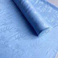 A roll of Bamboo Jacquard Mulberry Silk Fabric by Longan Craft, featuring a subtle colorful pattern, is partially unrolled on a flat surface.