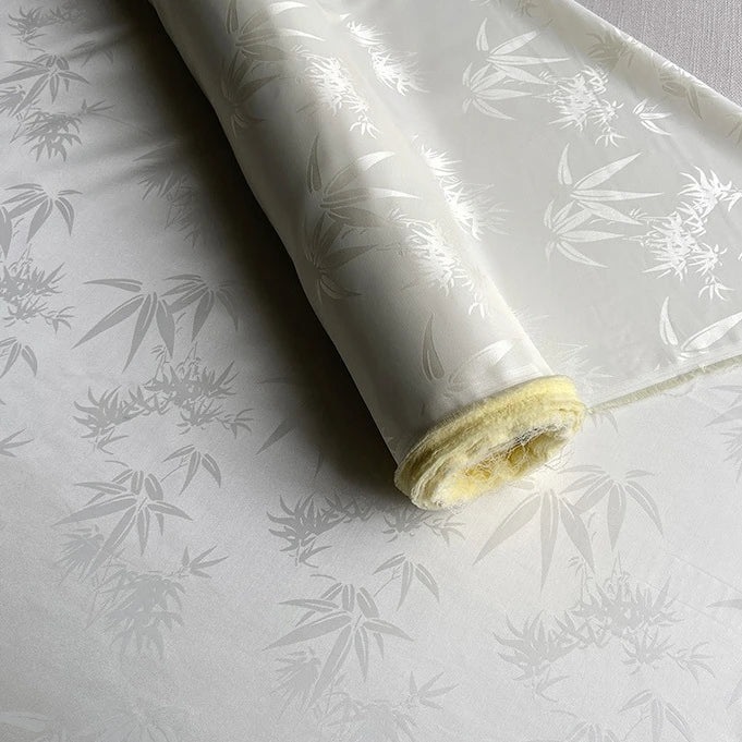 A partially unrolled roll of Bamboo Jacquard Mulberry Silk Fabric by Longan Craft, featuring a subtle floral pattern and slight sheen, shown in white as a cozy, elegant lining or colorful rayon silk fabric by the yard.