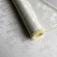 A partially unrolled roll of Bamboo Jacquard Mulberry Silk Fabric by Longan Craft, featuring a subtle floral pattern and slight sheen, shown in white as a cozy, elegant lining or colorful rayon silk fabric by the yard.