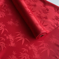 A roll of Bamboo Jacquard Mulberry Silk Fabric by Longan Craft, featuring a subtle, glossy floral and bamboo pattern, partially unrolled on a flat surface.