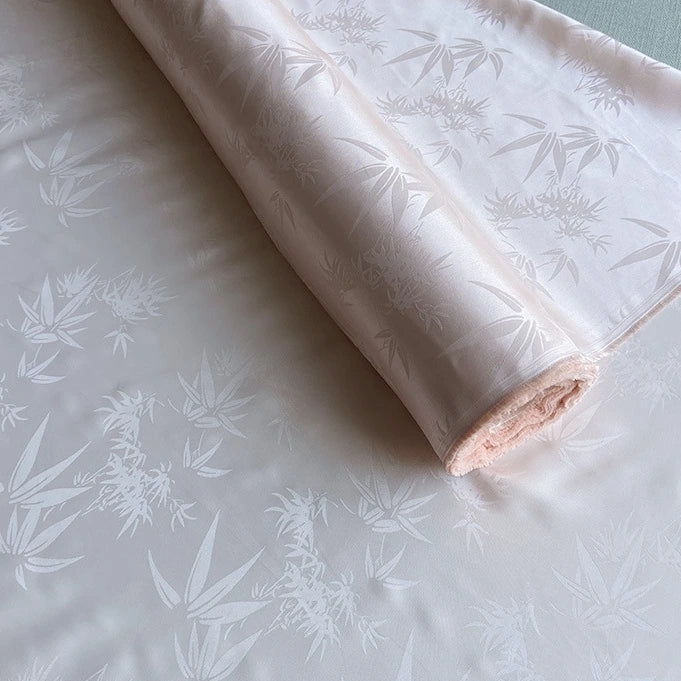 Longan Craft's Bamboo Jacquard Mulberry Silk Fabric By The Yard is partially unrolled, showcasing its silky, colorful rayon silk blend with a subtle glossy jacquard pattern—perfect for an elegant, cozy silk lining.