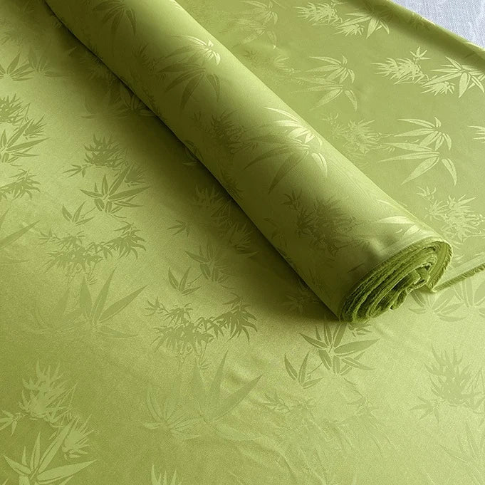 A partially unrolled piece of light green Bamboo Jacquard Mulberry Silk Fabric by Longan Craft, featuring a subtle woven pattern, is displayed on a flat surface.
