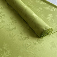 A partially unrolled piece of light green Bamboo Jacquard Mulberry Silk Fabric by Longan Craft, featuring a subtle woven pattern, is displayed on a flat surface.