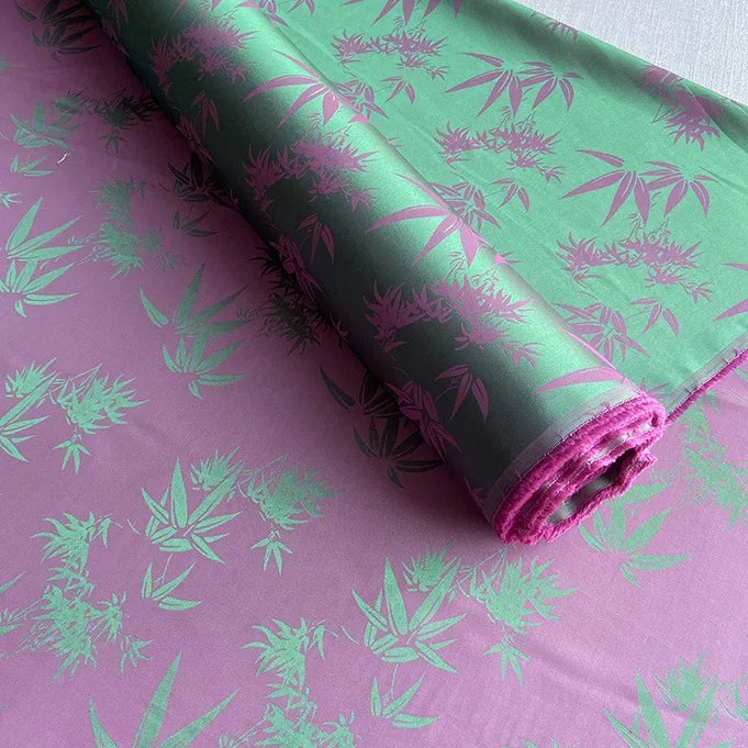 The Bamboo Jacquard Mulberry Silk Fabric by Longan Craft features a purple and green gradient with green bamboo leaves, made from a soft, slightly shiny mulberry silk blend—ideal as colorful rayon silk fabric or cozy silk lining.