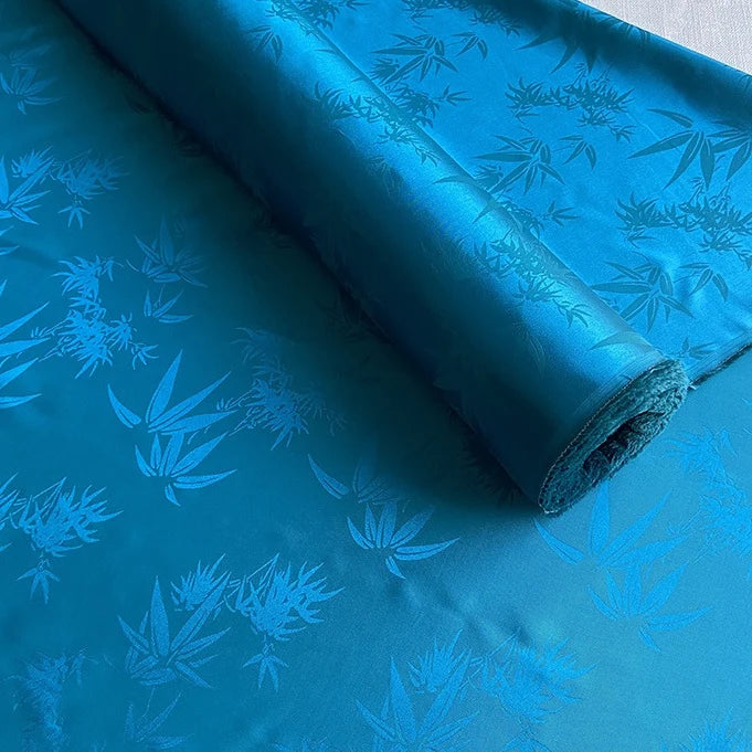 A partially unrolled piece of Bamboo Jacquard Mulberry Silk Fabric by Longan Craft, featuring a colorful embossed leaf pattern, displayed on a flat surface.