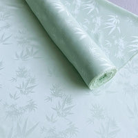 Longan Craft's Bamboo Jacquard Mulberry Silk Fabric by the yard is unrolled, showcasing a subtle leaf and floral pattern in light green. The colorful rayon silk looks smooth, delicate, and has a soft sheen—perfect as a cozy silk lining fabric.