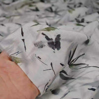 A hand holds Longan Craft's Bamboo Printed Nylon Viscose Fabric by the yard, a lightweight, eco-friendly Chinoiserie viscose with a sheer white base and delicate black and green floral-leaf print, perfect for premium dressmaking.