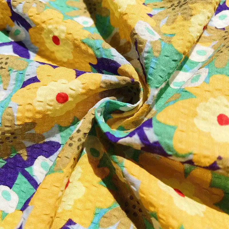 Close-up of Longan Craft’s Botanical Printed Seersucker Fabric By The Yard, a puckered cotton seersucker cloth featuring a vibrant floral pattern with yellow flowers, green leaves, and red centers, creating a textured and lively appearance—perfect for spring and summer skirts.