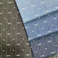 Four pieces of Longan Craft Bow Heart Jacquard Denim Fabric by the yard in blue and black, each with soft, washed cotton and neat vertical stripes featuring charming white bow and heart motifs—ideal for pants or crafts.