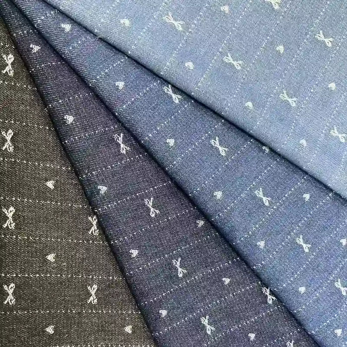 Four pieces of Bow Heart Jacquard Denim Fabric by Longan Craft in blue and black shades, featuring small white scissors and dotted line square patterns. The striped cotton-polyester blend denim is arranged overlapping diagonally.