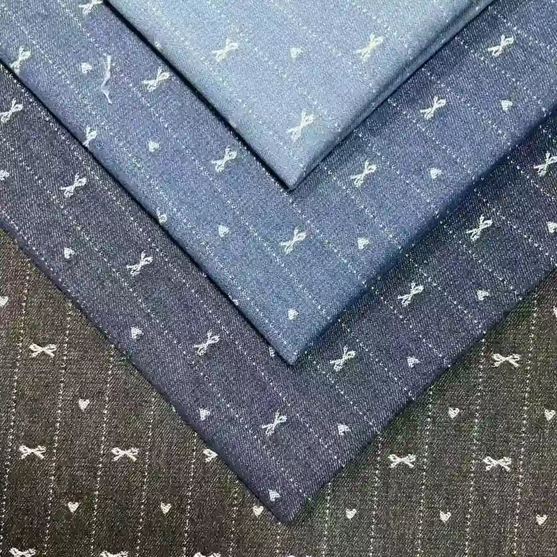 Four folded pieces of Longan Craft Bow Heart Jacquard Denim Fabric are stacked, each with a charming bow and heart pattern on blue and gray striped washed cotton-polyester denim—ideal for pants.