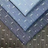 Four folded pieces of Longan Craft Bow Heart Jacquard Denim Fabric are stacked, each with a charming bow and heart pattern on blue and gray striped washed cotton-polyester denim—ideal for pants.