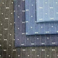 Four pieces of Longan Craft Bow Heart Jacquard Denim Fabric By The Yard in various blue and black shades overlap, each with a charming bow and heart pattern and dotted stripes, crafted from soft washed cotton denim for pants.
