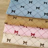 Four folded pieces of Longan craft Bow Plaid Print Corduroy Fabric By The Yard in blue, tan, pink, and cream—each showcasing a diamond grid plaid pattern with small bow designs—are stacked neatly on a wooden surface. This heavyweight checked printed corduroy material is both soft and durable, ideal for clothing projects.