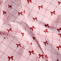 Bow Plaid Print Corduroy Fabric By The Yard from Longan craft is a heavyweight, soft, and durable corduroy material featuring a textured pink surface adorned with a repeating pattern of red bows and intersecting dashed red lines that form a charming diamond grid. The checked printed corduroy is gently folded, highlighting subtle shadows and its unique bow plaid design—perfect for clothing and crafts.
