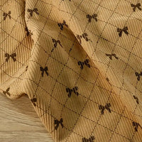Longan craft’s Bow Plaid Print Corduroy Fabric By The Yard—a heavyweight, soft, and durable checked printed corduroy material—features a beige background with a brown diamond grid pattern and small bow designs at each intersection, elegantly draped on a light wood surface.