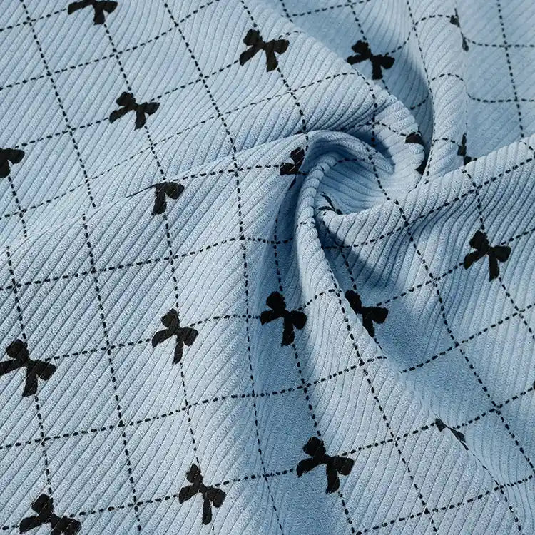 The Light Blue Bow Plaid Print Corduroy Fabric by Longan craft features a classic black grid pattern with small black bows at each intersection, shown here loosely gathered in the center. This heavyweight, soft, and durable checked corduroy material is ideal for clothing and is available by the yard.