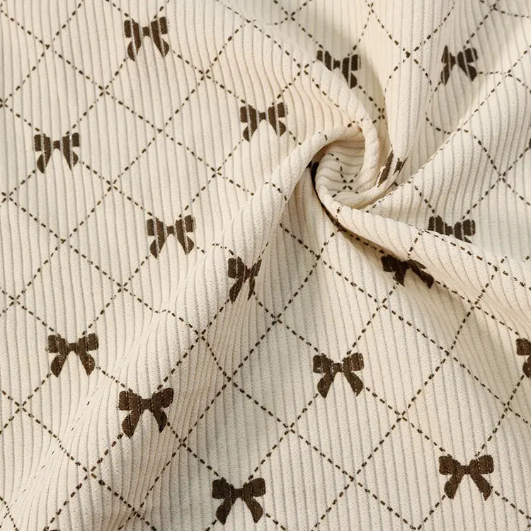 Showcasing the distinctive charm of Longan craft’s Bow Plaid Print Corduroy Fabric By The Yard, this heavyweight checked corduroy features a cream-colored ribbed texture adorned with a grid pattern and delicate brown bows at each intersection. Slightly twisted in the center, the soft and durable material beautifully highlights its rich texture and flexibility—making it an ideal choice for corduroy clothing projects.