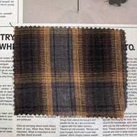 A rectangular swatch of Longan Craft’s Brown Plaid Cotton Flannel Fabric By The Yard—a lightweight, polyester brushed flannel material ideal for casual pants—is displayed on top of a newspaper page with visible black text.