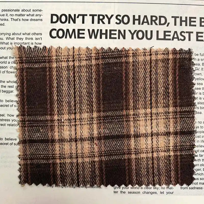 A piece of Longan Craft Brown Plaid Cotton Flannel Fabric By The Yard is laid atop a printed page featuring large, bold text and smaller paragraphs.