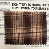 A piece of Longan Craft Brown Plaid Cotton Flannel Fabric By The Yard is laid atop a printed page featuring large, bold text and smaller paragraphs.