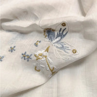 A close-up of Longan Craft’s Butterfly Floral Embroidered Ramie Fabric By The Yard, showing delicate embroidery with a blue and white butterfly, small blue flowers, and white blossoms on thin 100% ramie material for soft dresses.