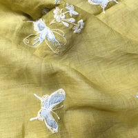 Close-up of Longan Craft's Butterfly Floral Embroidered Ramie Fabric By The Yard, featuring light yellow thin 100 ramie with delicate white and pale blue butterfly and floral embroidery, showing its soft texture and intricate stitching for dresses.