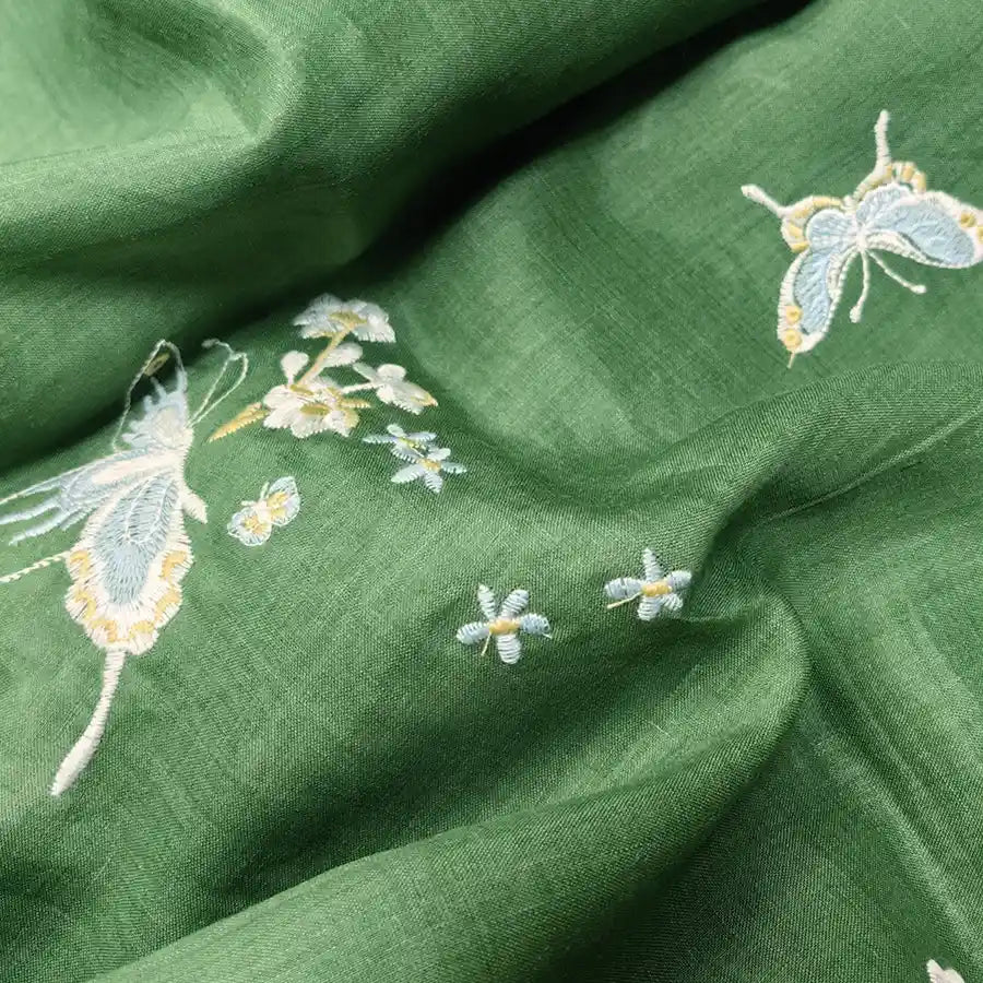 Longan Craft's Butterfly Floral Embroidered Ramie Fabric features light blue and yellow butterflies with white flowers on green eco-friendly ramie, perfect for soft dresses and sewing projects.