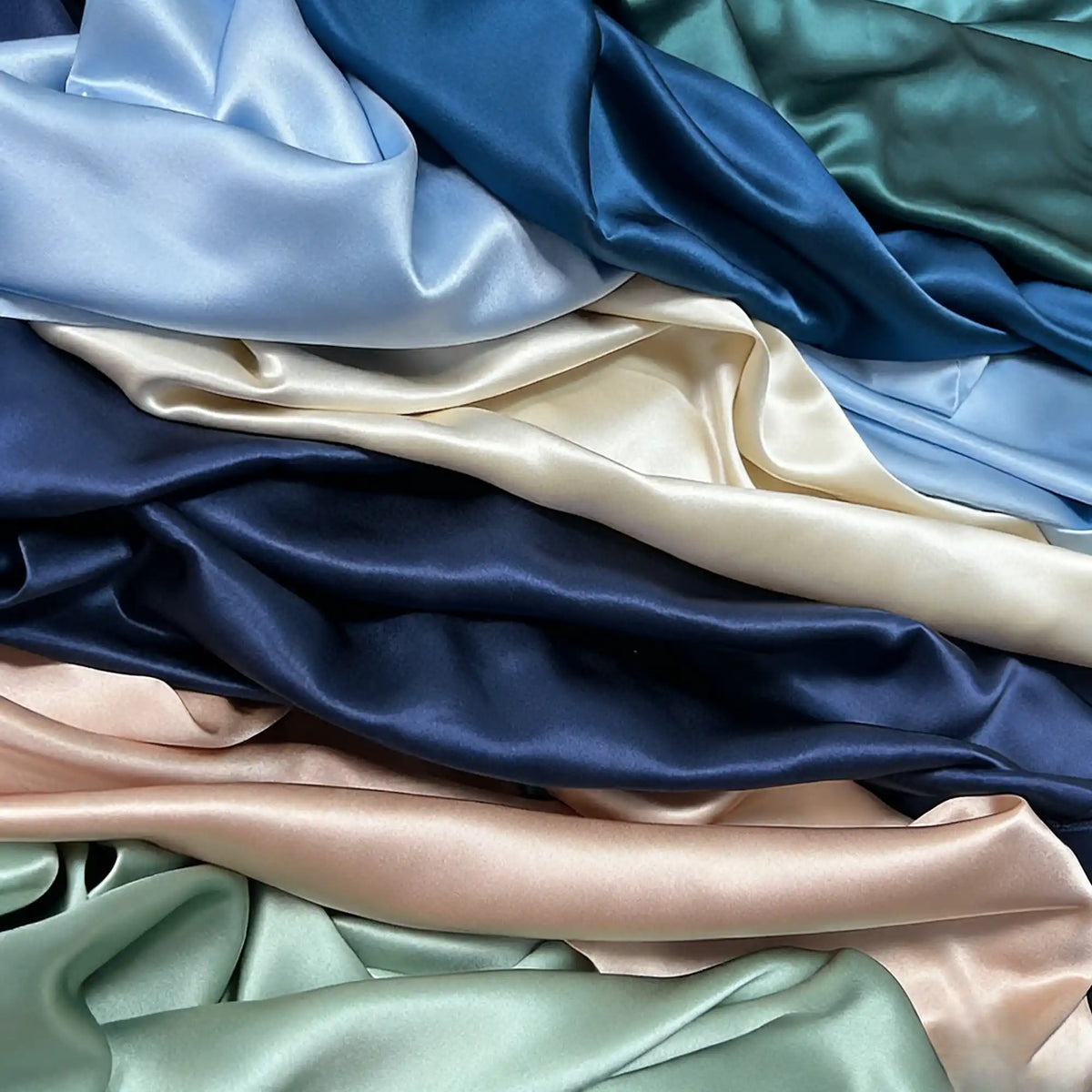 Longan Craft’s Charmeuse Silk Fabric by the yard features luxurious mulberry silk satin in solid blue, green, cream, and peach shades, beautifully draped in soft, flowing folds—perfect for bridal and special creations.