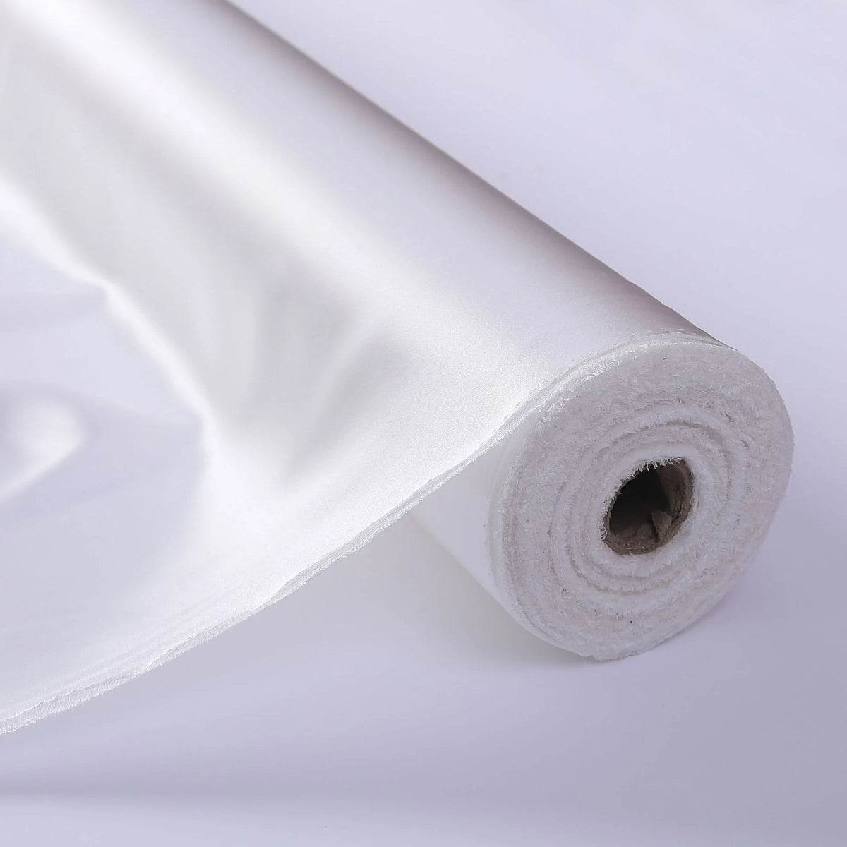 A close-up of a roll of Longan Craft Charmeuse Silk Fabric By The Yard in solid white Mulberry silk satin, partially unrolled to showcase its luxurious, shiny texture—ideal for elegant bridal wear.