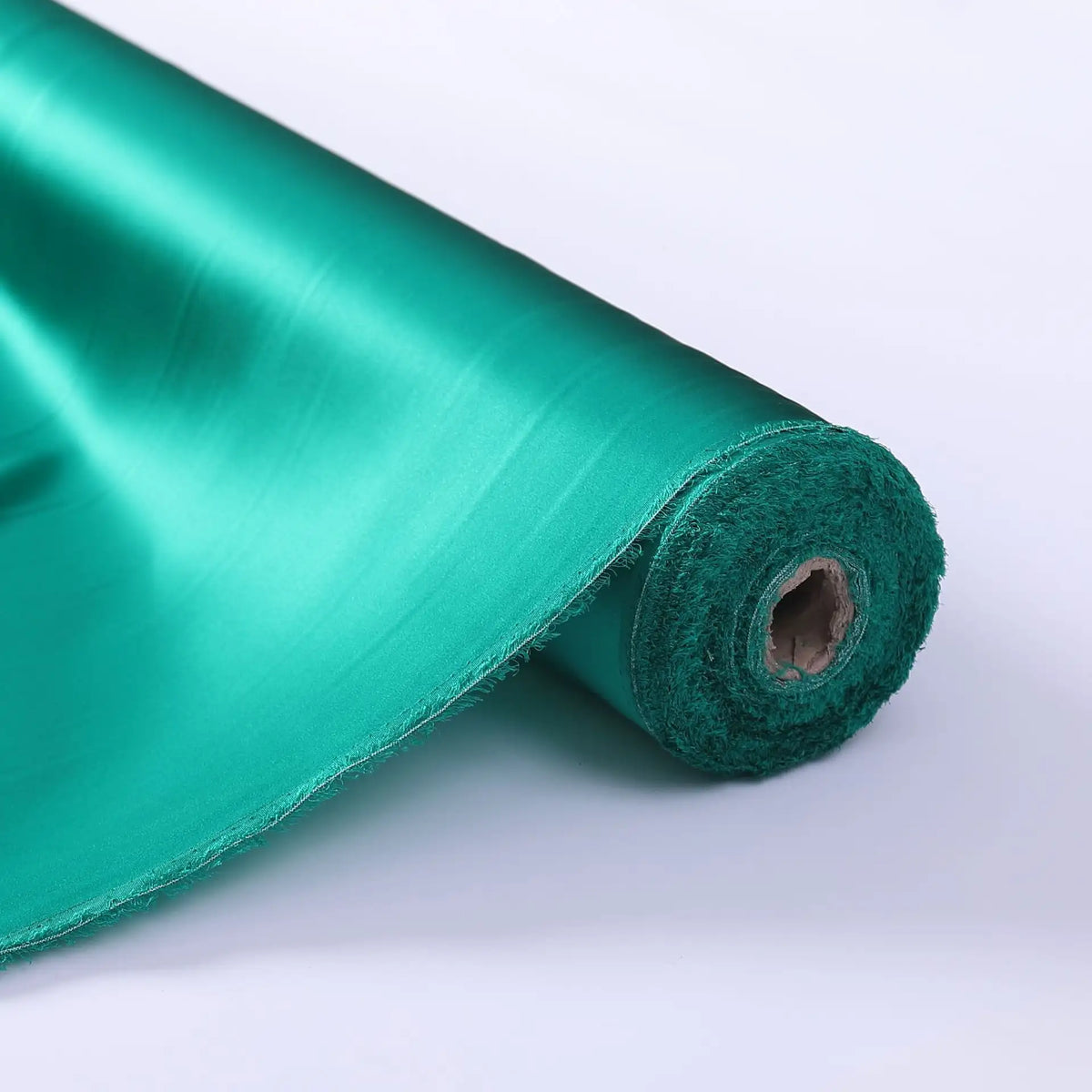 A roll of Longan Craft Charmeuse Silk Fabric By The Yard in shiny green Mulberry silk satin is partially unrolled on a white surface, showing its smooth, glossy texture—perfect for luxurious bridal wear.