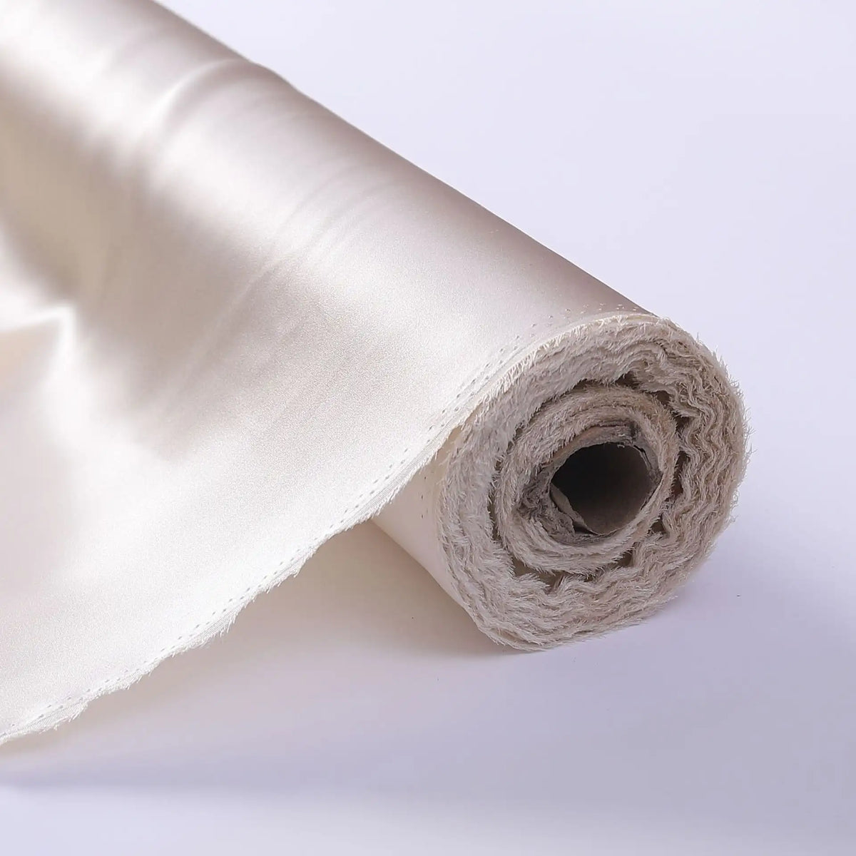 A close-up of Longan Craft's Charmeuse Silk Fabric By The Yard—luxurious off-white mulberry silk satin, partially unrolled on a flat surface—ideal for elegant bridal creations.