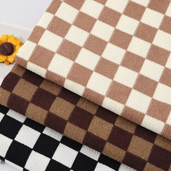 Three folded Longan Craft Checkered Corduroy Fabrics in cream and brown, brown and dark brown, and black and white patterns. Soft printed polyester corduroy for apparel with a visible yellow artificial flower at the corner.