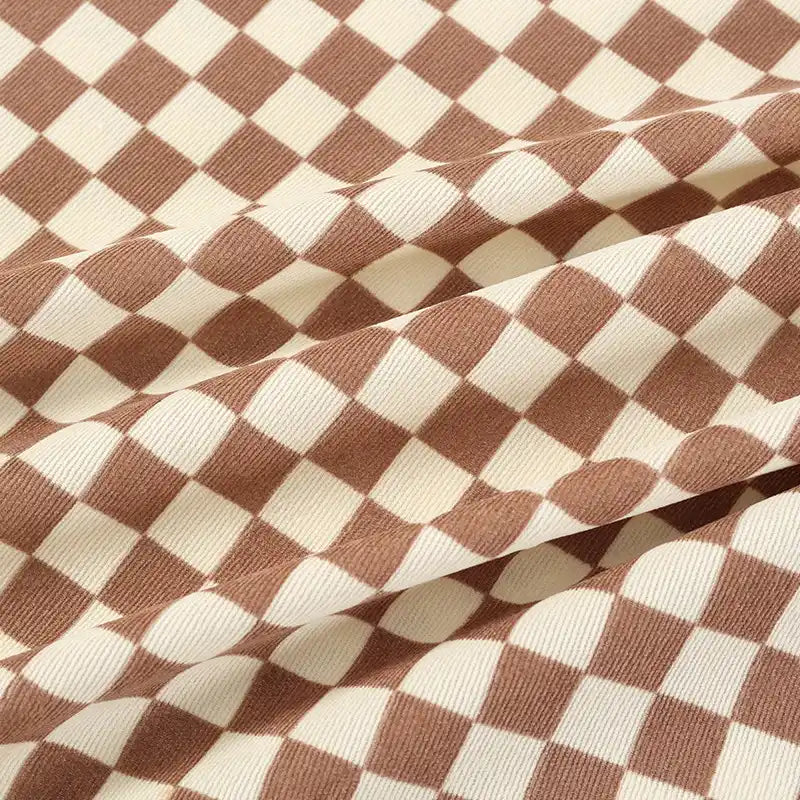 Close-up of Longan Craft's Checkered Corduroy Fabric By The Yard shows its soft, durable printed polyester in a brown and beige checkerboard. Ribbed texture and visible folds create depth, highlighting this unique fabric for apparel.