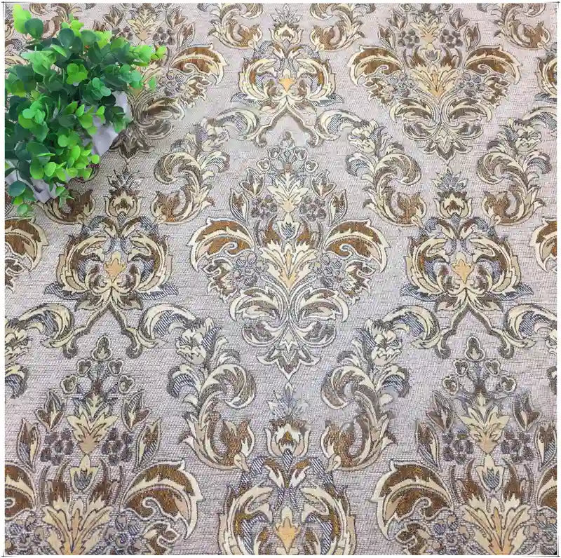 Longan Craft's Chenille Damask Fabric by the Yard features an ornate vintage-style floral and leaf jacquard design in beige, brown, and gold tones; a small green leafy plant sits in the upper left corner.