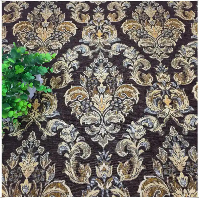 A leafy green plant rests on a brown surface with an ornate gold and beige floral pattern, created from Longan Craft’s Chenille Damask Fabric By The Yard—an elegant floral jacquard upholstery fabric.