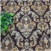A leafy green plant rests on a brown surface with an ornate gold and beige floral pattern, created from Longan Craft’s Chenille Damask Fabric By The Yard—an elegant floral jacquard upholstery fabric.