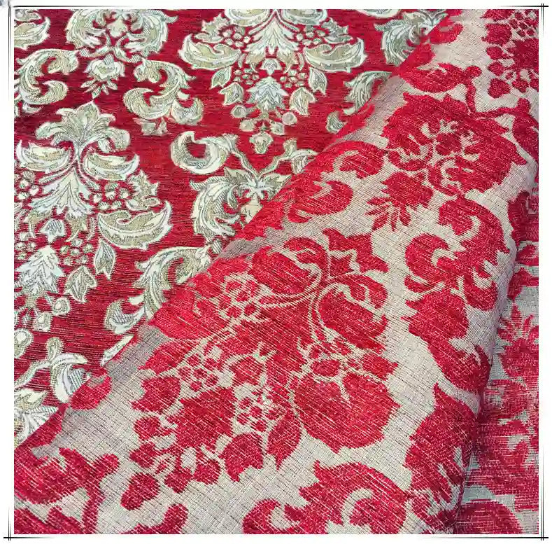 A close-up of Longan Craft’s Chenille Damask Fabric by the Yard shows its ornate red and gold floral jacquard pattern. A section is folded, revealing the reverse side with a muted red and beige design—perfect for upholstery projects.
