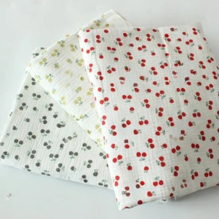 Three pieces of Longon Craft Cherry Print Double Gauze Fabric feature red, yellow, and gray cherries on white soft muslin cotton—perfect for children’s clothing. Overlapped on a flat surface, this fabric is ideal for sewing projects.