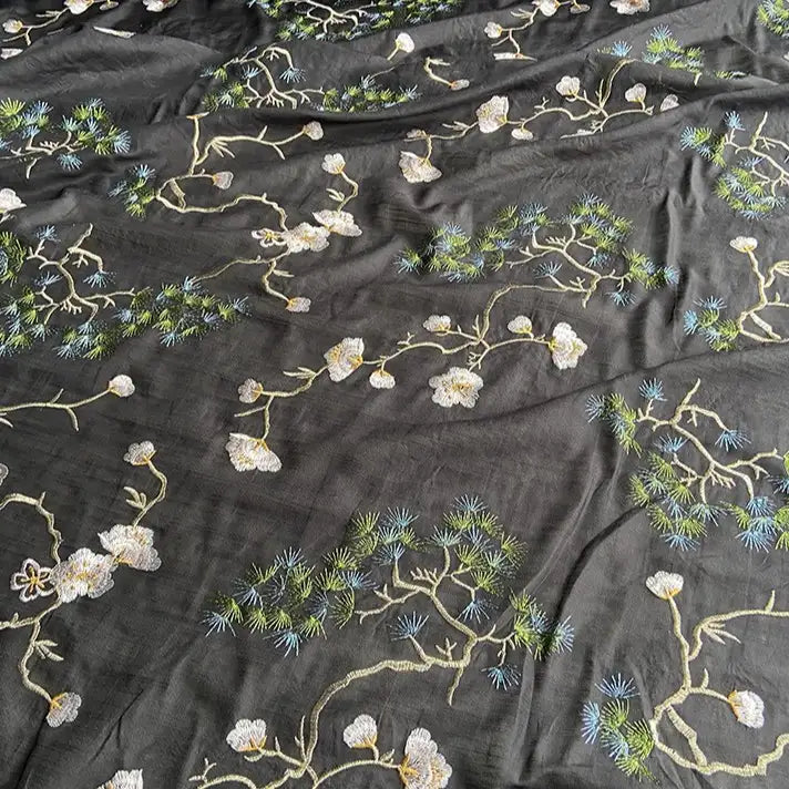 The Longan Craft Chinoiserie Embroidered Silk Fabric by the yard features a sheer black cotton-mulberry silk blend with delicate white flowers and green pine branch embroidery—perfect for elegant, nature-inspired blouses.