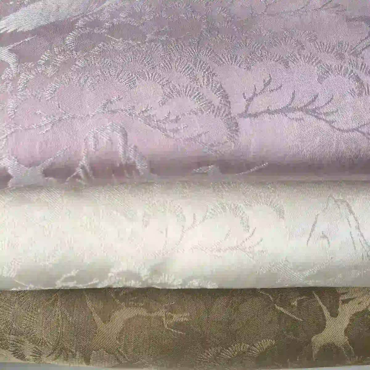 Three folded Chinoiserie Polyester Viscose Fabrics by Longan Craft, in pale lavender, ivory, and beige with a woven deer and botanical pattern, showcase refined jacquard style—perfect as curtain material by the yard.