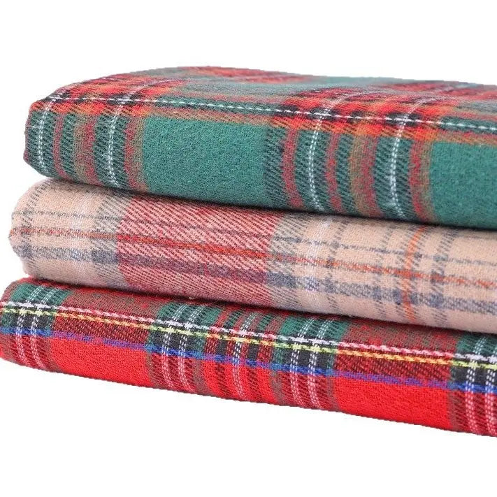 Three folded wool fabrics with plaid patterns are stacked: the top features green with red and white lines, the middle showcases beige with red and gray stripes, and the bottom displays red with green and blue stripes. These timeless designs from Longan Craft’s “Christmas Plaid Sueded Flannel Fabric By The Yard” collection are perfect choices for holiday sewing projects or cozy brushed flannel crafts, making them ideal checked holiday flannel material for classic dresses or festive décor.