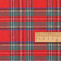 A wooden ruler marked in centimeters rests on the Christmas Plaid Sueded Flannel Fabric By The Yard from Longan Craft, highlighting the bold red, green, and white checked holiday pattern. The scale demonstrates the detailed weave and vibrant colors of this brushed flannel textile—ideal for classic dresses or festive sewing projects.