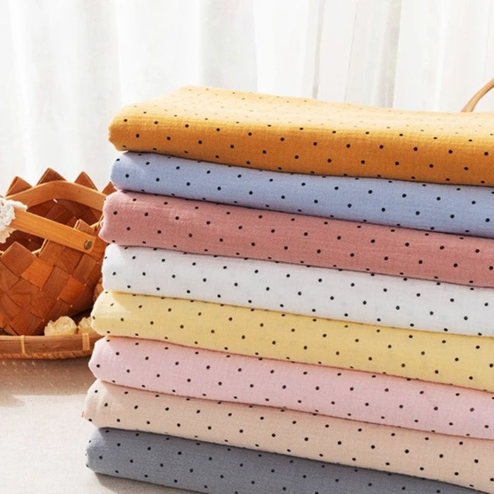 A stack of Longan Craft Classic Small Polka Dot Gauze Fabric (100% cotton double gauze), perfect for baby clothing and pajamas, is folded on a table near a woven basket.