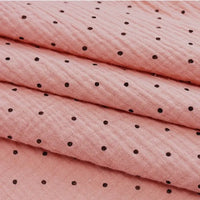 A close-up of Longan Craft's Classic Small Polka Dot Gauze Fabric, a 100% cotton double gauze by the yard, shown folded in pink with black polka dots—perfect for baby clothing or pajamas.
