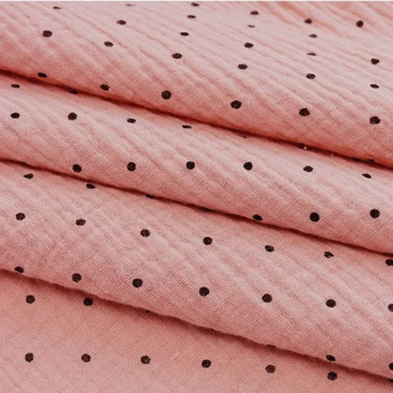 A close-up of Longan Craft's Classic Small Polka Dot Gauze Fabric, a 100% cotton double gauze by the yard, shown folded in pink with black polka dots—perfect for baby clothing or pajamas.