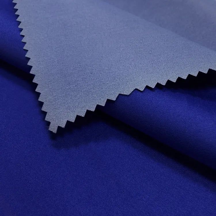 Two pieces of Longan Craft Coated Waterproof Peachskin Fabric are layered: the top is a lighter shade with zigzag edges, the bottom is darker royal blue with a smooth cozy texture. Both microfiber polyester layers offer excellent waterproof performance.
